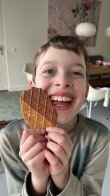 Laughing child holding a thin waffle biscuit with chocolate on one half