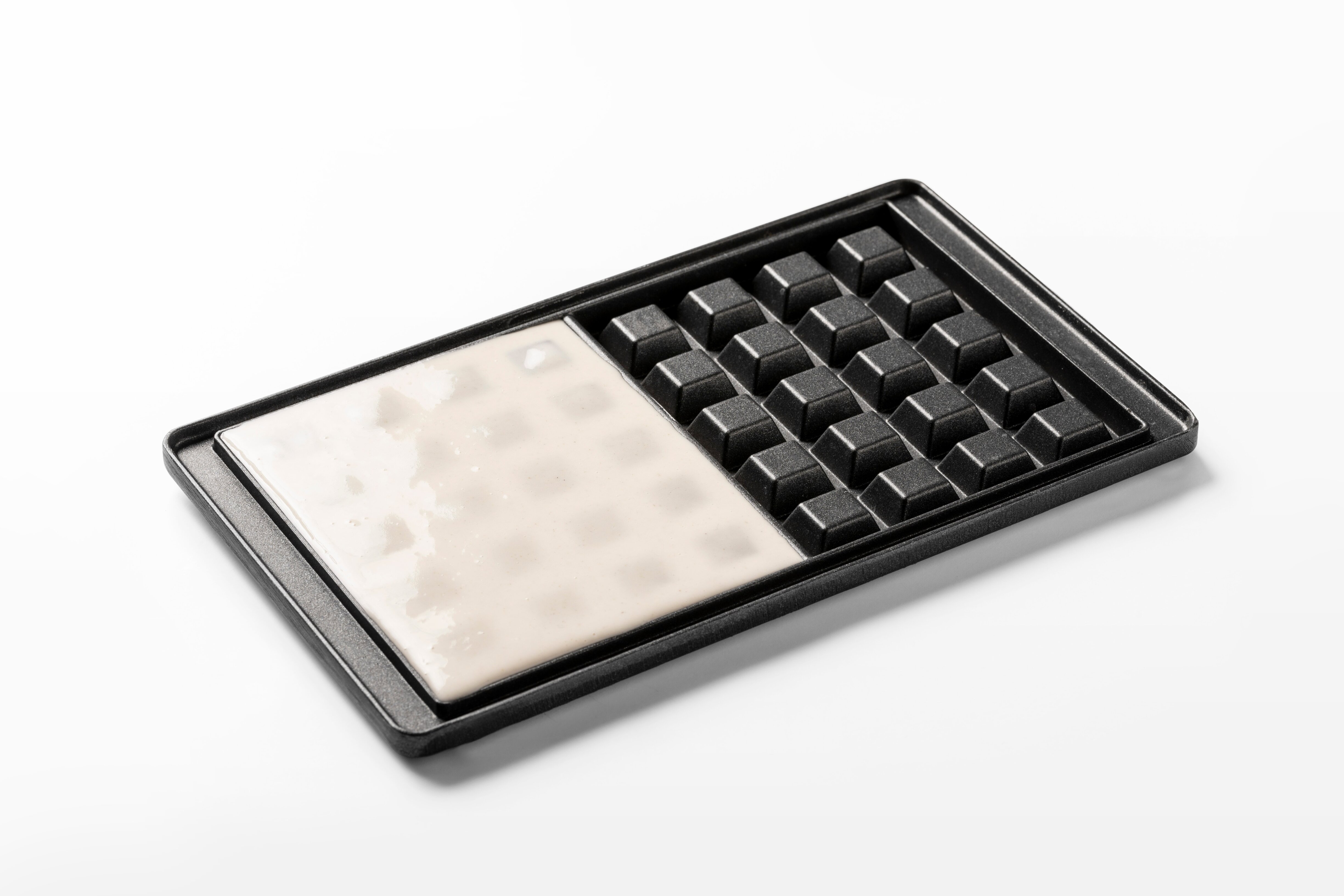 Waffle mould tray with white batter in one half and empty cells in the other