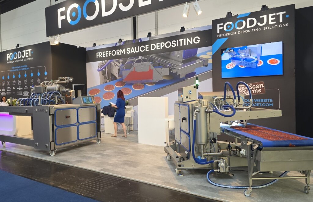 Depositing lines on the FoodJet stand at iba 2025, one depositing red sauce on pizza bases
